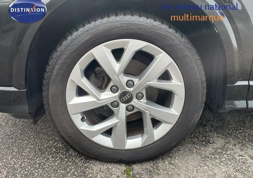 Gros plan sur la roue avant gauche d’un Audi Q2 noir mitto metal avec jante alu et logo Audi au centre.