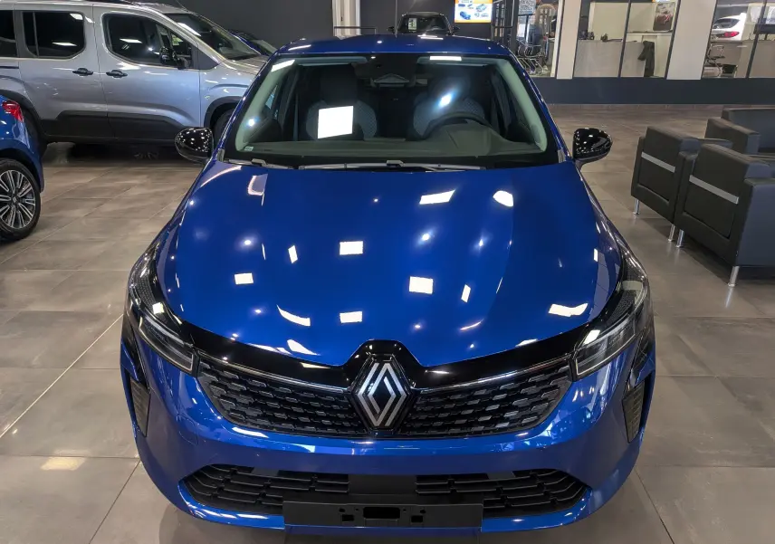 Vue avant d'une Renault Clio V Bleu Iron 2025 en concession, avec calandre noire et phares LED fins.