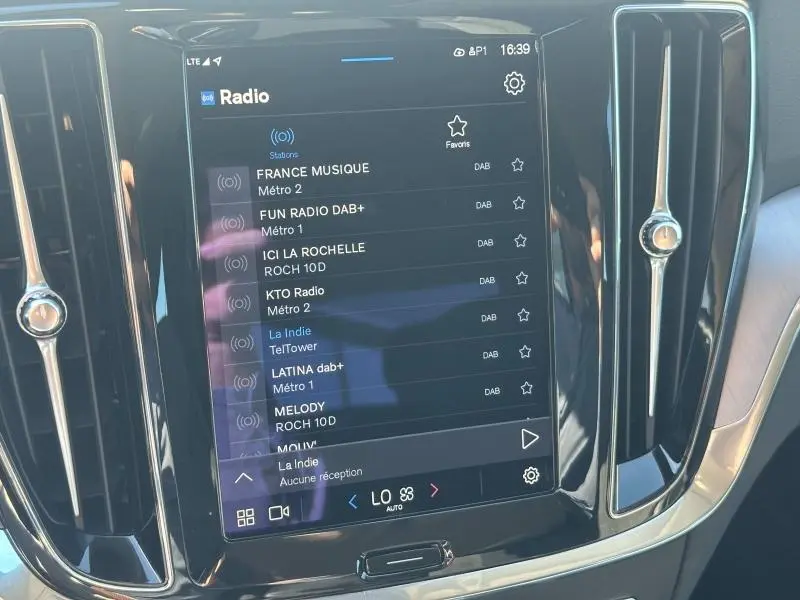 Écran tactile central de la Volvo S60 B4 2024 affichant les stations radio DAB, entouré de finitions noires brillantes.