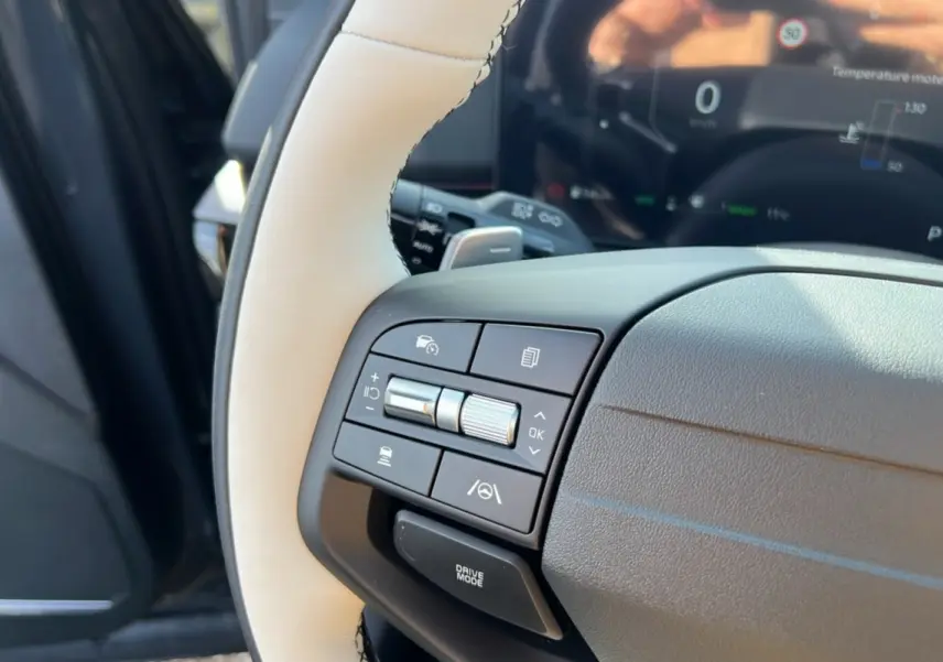 Gros plan sur le volant cuir beige et noir du Kia Sportage 2026, avec commandes multifonctions côté gauche et tableau de bord numérique.