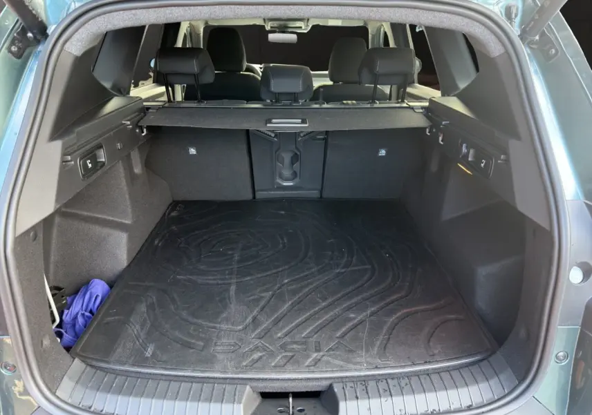 Coffre ouvert d'un Dacia Bigster vert, vue arrière montrant la grande capacité et le tapis de coffre noir marqué Dacia.