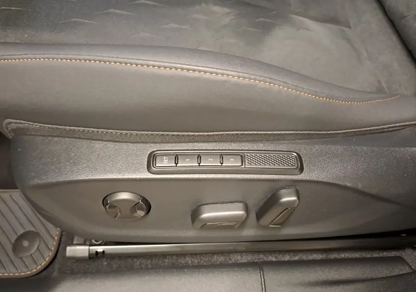 Détail des commandes de réglage électrique du siège conducteur avec surpiqûres orange dans l'habitacle du CUPRA TERRAMAR noir Minuit.