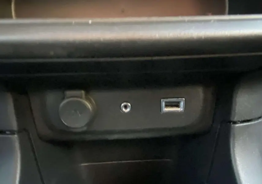 Gros plan sur les ports USB, prise jack et allume-cigare dans la console centrale d'une Citroën C3 noire toit rouge.