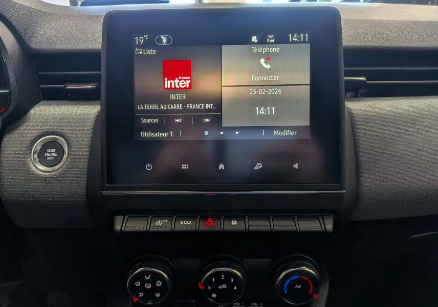 Vue rapprochée de l’écran tactile central et des commandes de climatisation d’une Renault Clio V Bleu Iron.