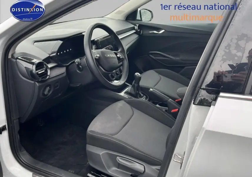 Intérieur vue côté conducteur d’une Skoda Fabia blanche 2025, volant cuir et boîte manuelle visibles.