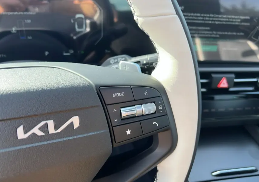 Gros plan sur le volant cuir blanc de la Kia Sportage 2026 avec commandes multifonctions et tableau de bord numérique flou.