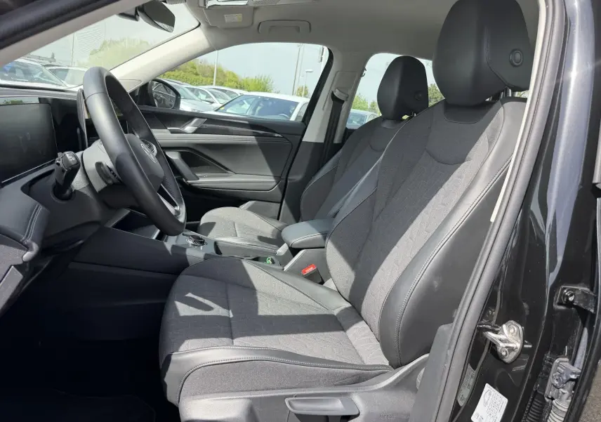 Vue intérieure côté conducteur du Volkswagen Tiguan 2025 noir, sièges tissu et cuir gris, volant multifonction en cuir.