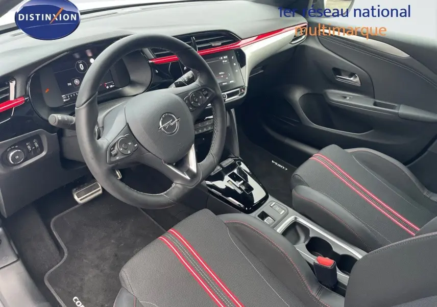 Intérieur avant droit de l'Opel Corsa blanc 2022, avec volant multifonction et sièges noirs à surpiqûres rouges.