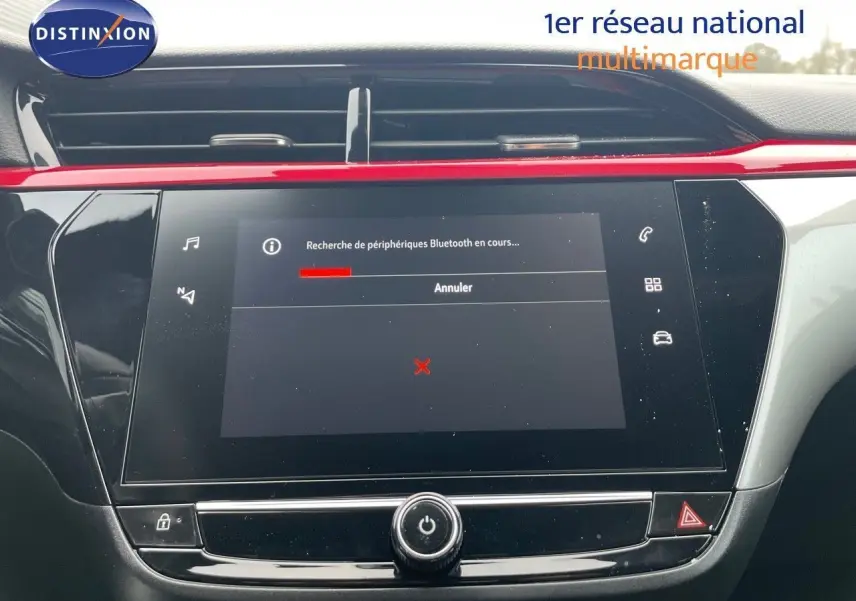 Écran tactile central de la console d'une Opel Corsa blanche, avec une barre rouge décorative au-dessus.