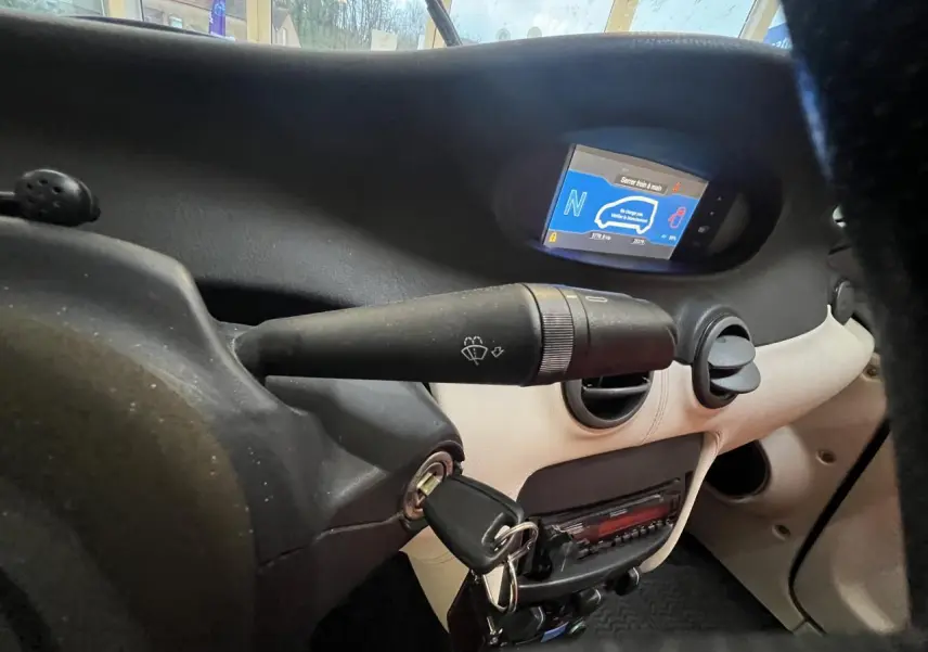 Vue rapprochée du tableau de bord beige et noir du Citroën E-MEHARI cabriolet 2016 avec clé insérée et écran digital allumé.