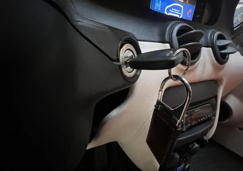 Gros plan intérieur sur le tableau de bord beige et noir du Citroën E-MEHARI cabriolet bleu clair avec clé insérée dans le contacteur.