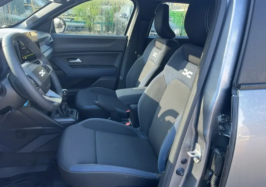 Vue intérieure côté conducteur du Dacia Duster 2025 gris schiste, montrant les sièges avec logo Expression et levier de vitesses manuel.