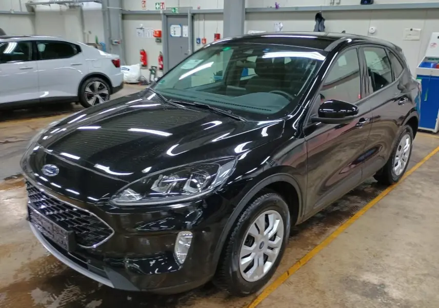 Ford Kuga noir Obsidien vu en 3/4 avant droit dans un garage, mettant en valeur ses phares et sa calandre.