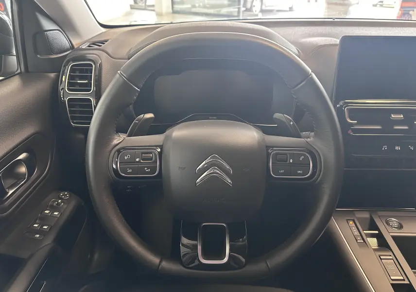 Vue intérieure centrée sur le volant cuir du Citroën C5 Aircross 2024 avec commandes intégrées et tableau de bord numérique.