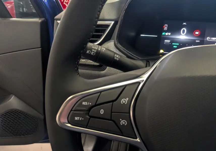 Gros plan sur le volant de la Renault Clio V Bleu Iron, montrant les commandes de régulateur de vitesse et l'écran digital.