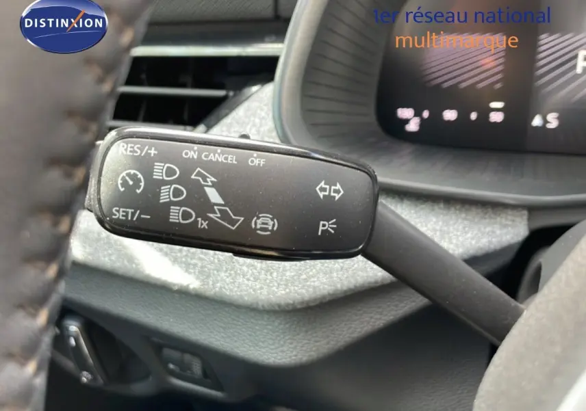 Gros plan sur la commande de régulateur de vitesse à gauche du volant dans l’habitacle gris noir d’une Skoda Scala blanc glacier 2025.