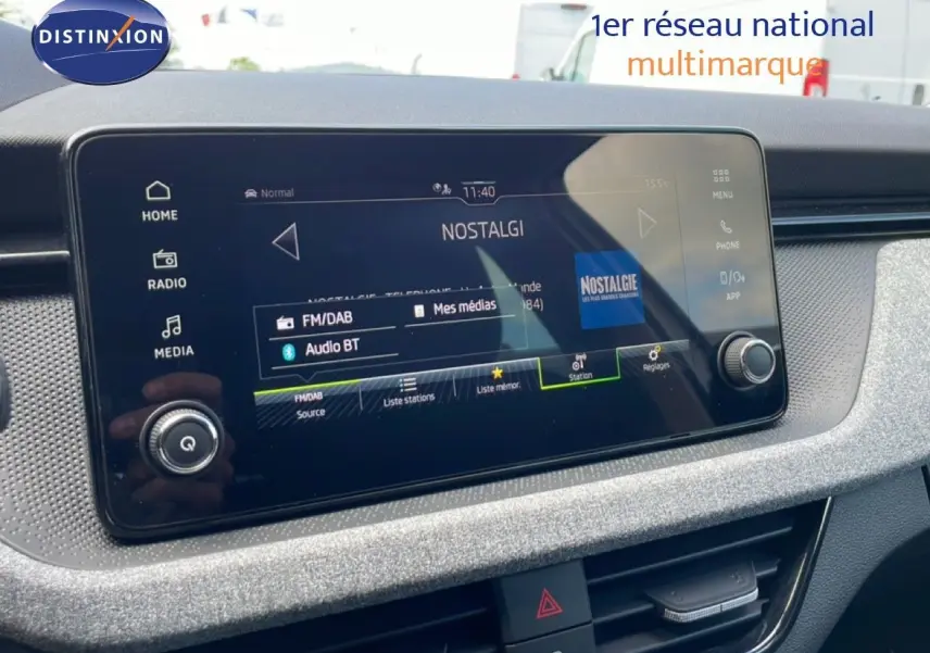 Écran tactile central du tableau de bord du Skoda Scala blanc glacier, affichant la radio Nostalgie en mode FM/DAB.