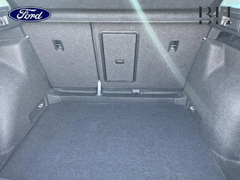 Coffre vide vu de l'intérieur d'un véhicule, revêtement gris foncé, avec trappe centrale et fixations Isofix.