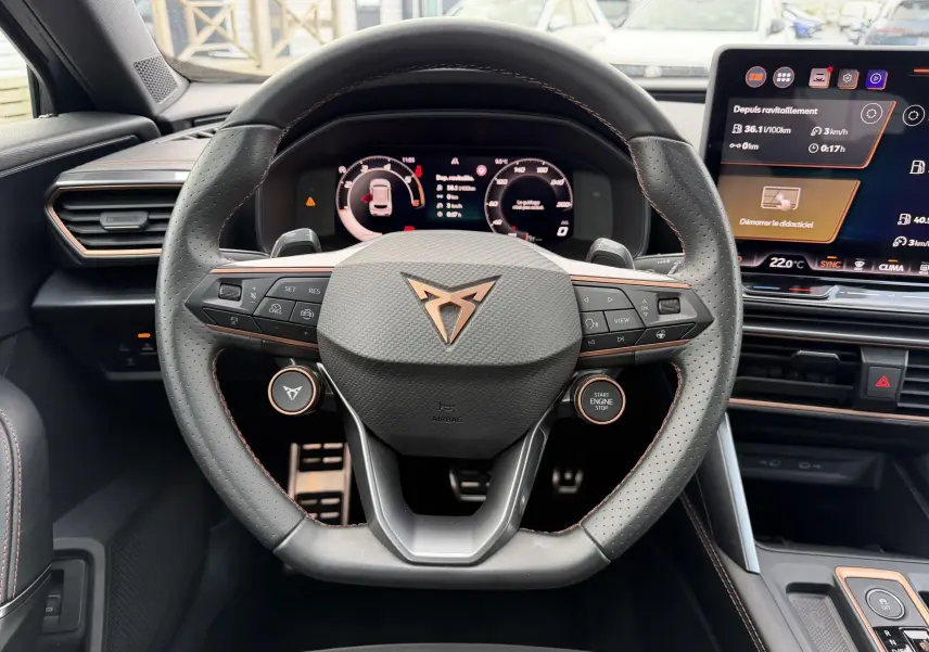 Vue intérieure centrée sur le volant cuir perforé noir avec logo CUPRA cuivré et tableau de bord digital lumineux.