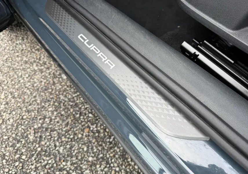 Gros plan sur la plaque de seuil de porte côté gauche bleu métallisé avec logo CUPRA blanc visible.