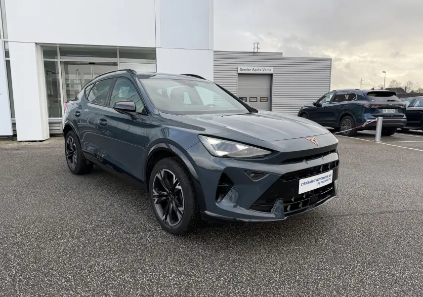 Vue 3/4 avant droit d'un CUPRA Formentor bleu métallisé avec jantes noires, garé devant un bâtiment commercial.