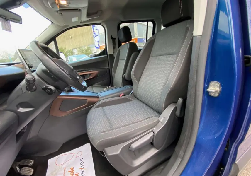 Intérieur avant du Peugeot Rifter bleu 2023, sièges tissu gris avec surpiqûres et tableau de bord visible côté conducteur.