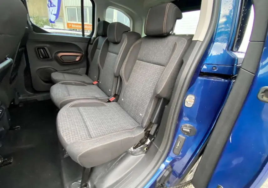 Vue latérale intérieure sur les sièges arrière gris à motifs du Peugeot Rifter GT bleu, porte ouverte côté droit.