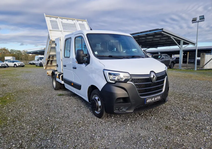 Renault Master blanc en 3/4 avant droit avec benne relevée et cabine double sur parking extérieur.