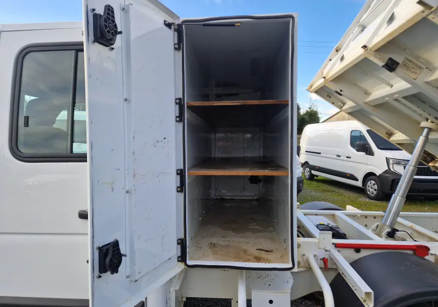 Vue latérale gauche du Renault Master blanc 2023 avec benne relevée et coffre de rangement ouvert montrant ses étagères.