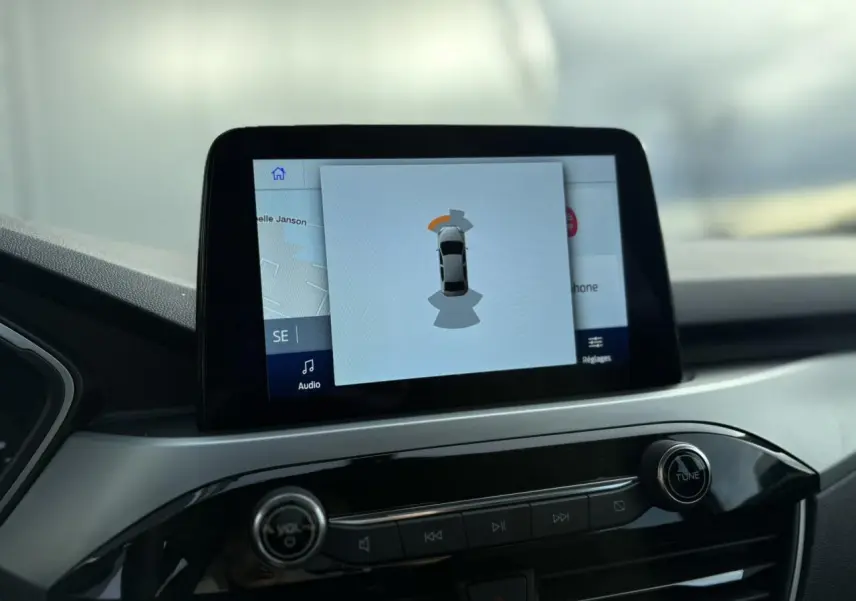 Écran tactile central du Ford Kuga 2024 affichant l'aide au stationnement avec interface moderne et tableau de bord noir.