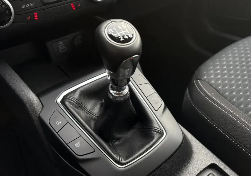 Gros plan sur la boîte manuelle et le levier de vitesse en cuir noir du Ford Kuga 2024, avec siège avant gris à motifs.