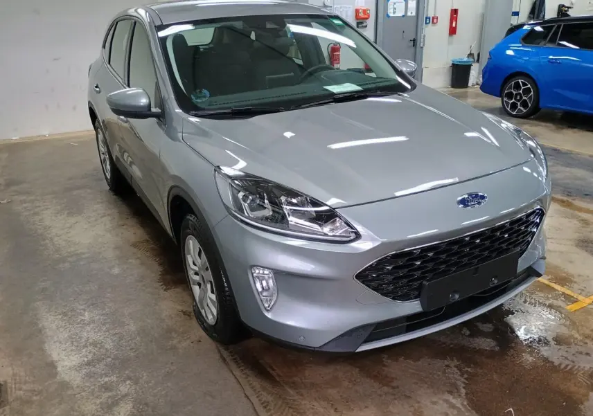 Ford Kuga gris Solar vu en 3/4 avant droit dans un garage, avec calandre noire et phares modernes.
