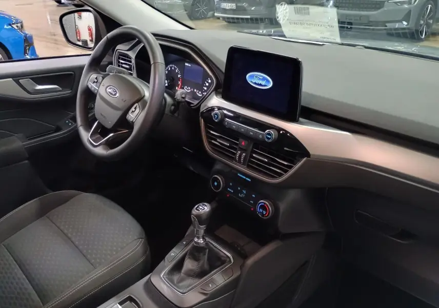 Vue intérieure côté conducteur du Ford Kuga 2024 avec tableau de bord moderne et écran tactile affichant le logo Ford.