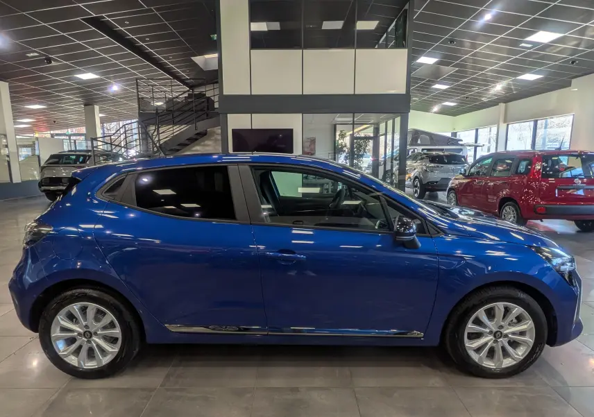 Profil côté gauche d'une Renault Clio V Bleu Iron 2025 en intérieur, avec jantes alliage et vitres teintées.