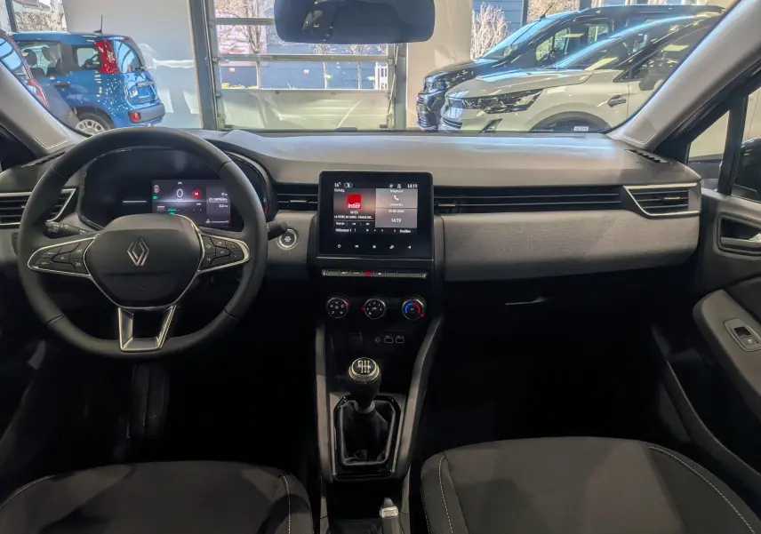 Vue intérieure avant de la Renault Clio V 2025, tableau de bord moderne avec écran tactile et volant multifonction.