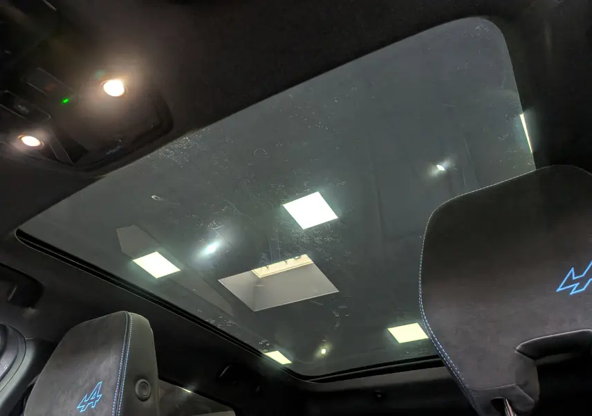 Vue intérieure du toit panoramique du Renault Austral E-Tech hybrid 200 Iconic esprit Alpine avec sièges noirs et logo Alpine bleu.