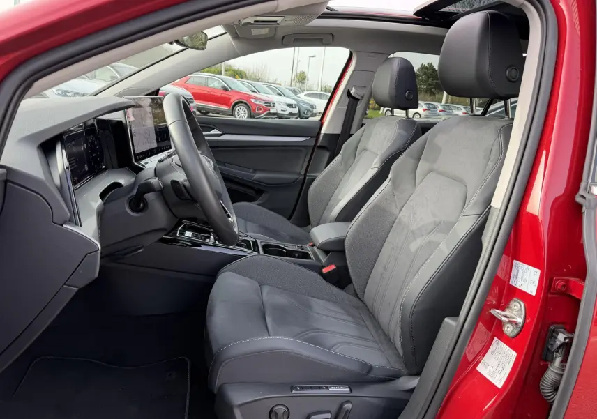 Vue intérieure côté conducteur de la Volkswagen Golf SW rouge 2025, avec sièges sport gris et tableau de bord digital.