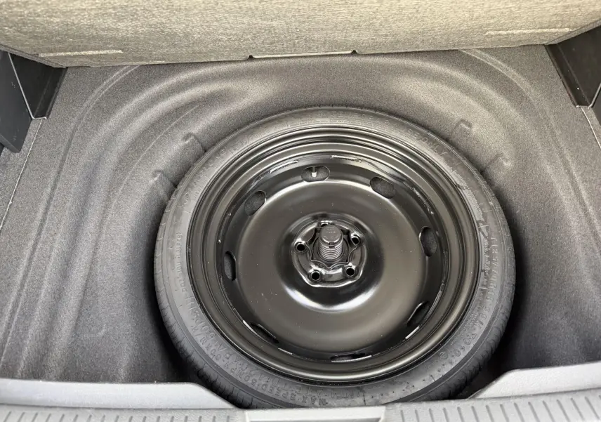 Gros plan sur la roue de secours compacte noire dans le coffre d’une Volkswagen Golf SW rouge.