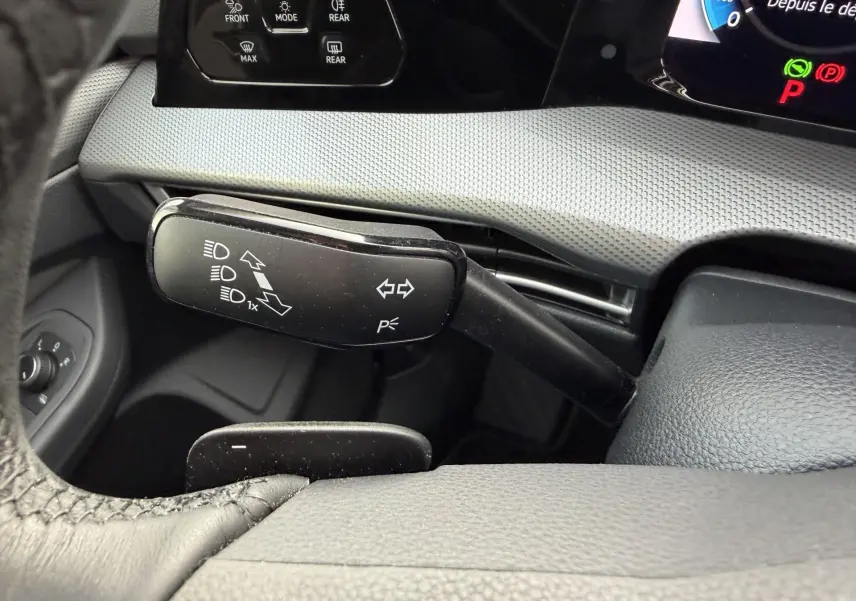 Gros plan sur la manette de clignotant noire à gauche du volant dans l’habitacle gris d’une Volkswagen Golf SW rouge.