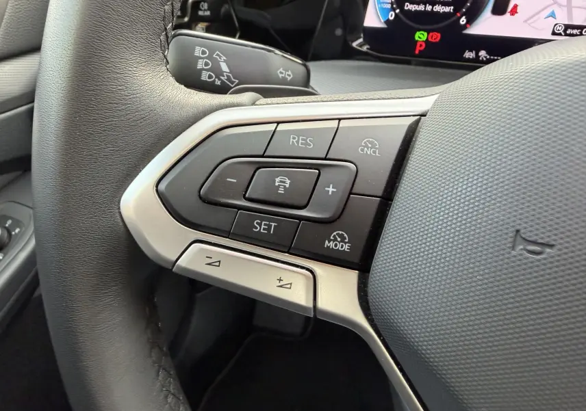 Gros plan sur les commandes au volant à gauche de la Volkswagen Golf SW rouge 2025, avec affichage digital en arrière-plan.