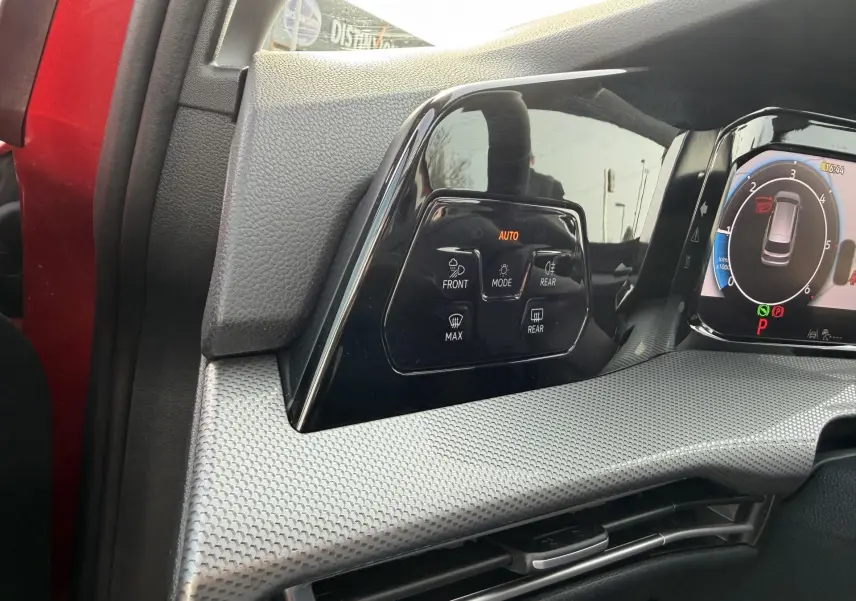 Détail du tableau de bord côté gauche de la Volkswagen Golf SW rouge 2025 avec commandes climatisation et écran digital.
