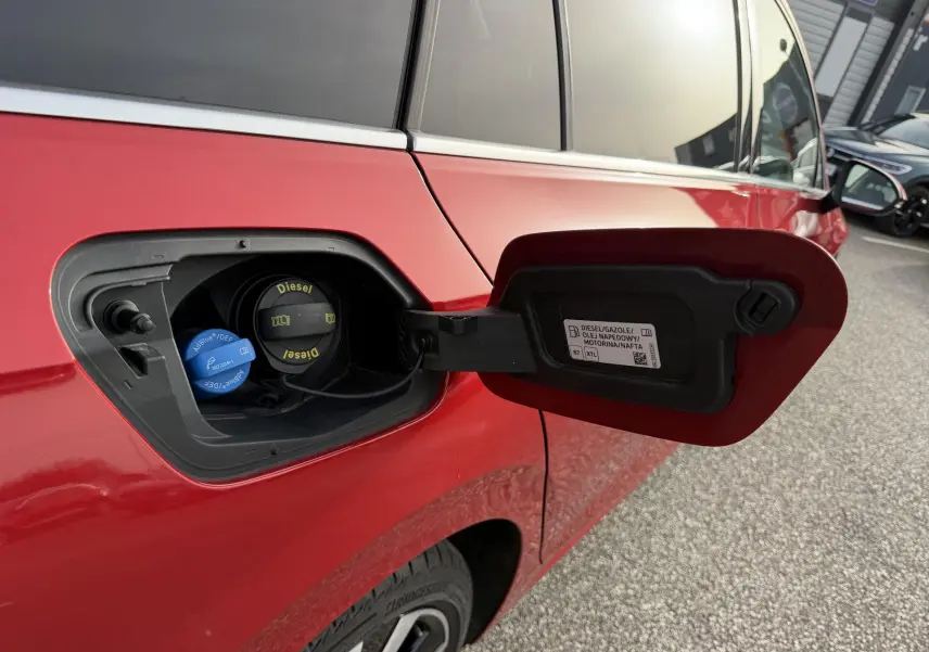 Détail de la trappe à carburant ouverte côté gauche d'une Volkswagen Golf SW rouge, montrant les bouchons Diesel et AdBlue.