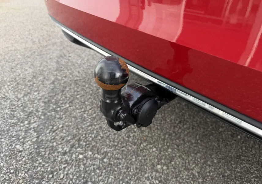Gros plan sur l'attelage rabattable noir avec boule usée sous le pare-chocs rouge métallisé d'une Volkswagen Golf SW.