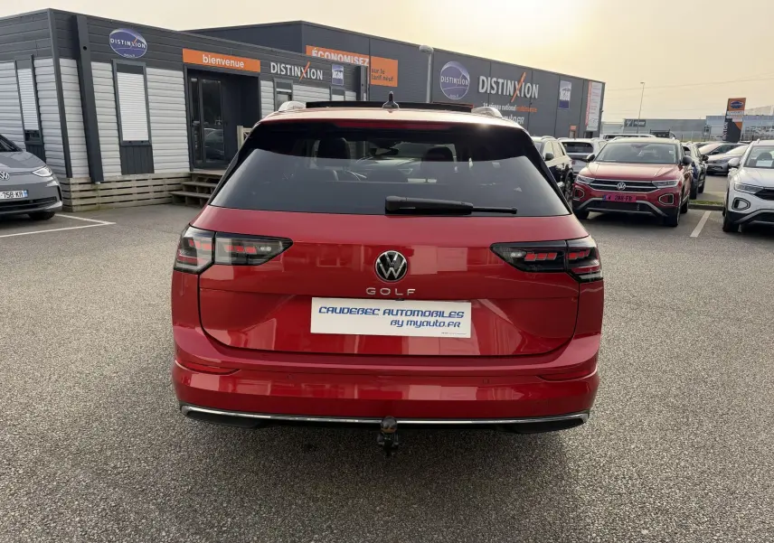 Vue arrière d'une Volkswagen Golf SW rouge avec attelage rabattable sur parking de concession.
