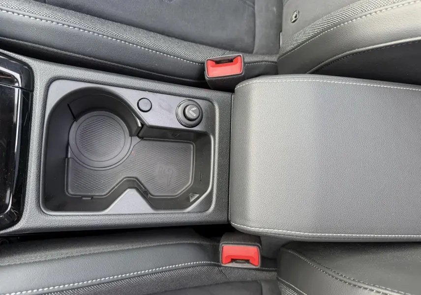 Gros plan sur la console centrale noire avec porte-gobelets et accoudoir gris, sièges tissu et cuir dans une Volkswagen Golf SW rouge.