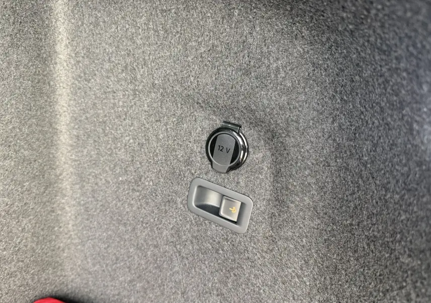 Détail de la prise 12V et levier de déverrouillage électrique de l'attelage dans le coffre de la Volkswagen Golf SW rouge.