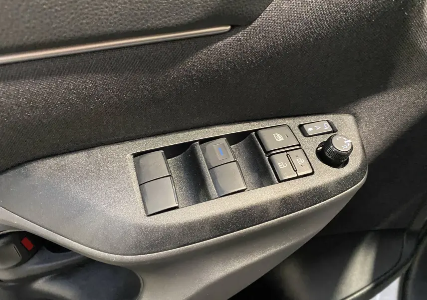 Gros plan sur les commandes de lève-vitres et rétroviseurs côté conducteur d'une Toyota Yaris Cross blanche, intérieur noir.