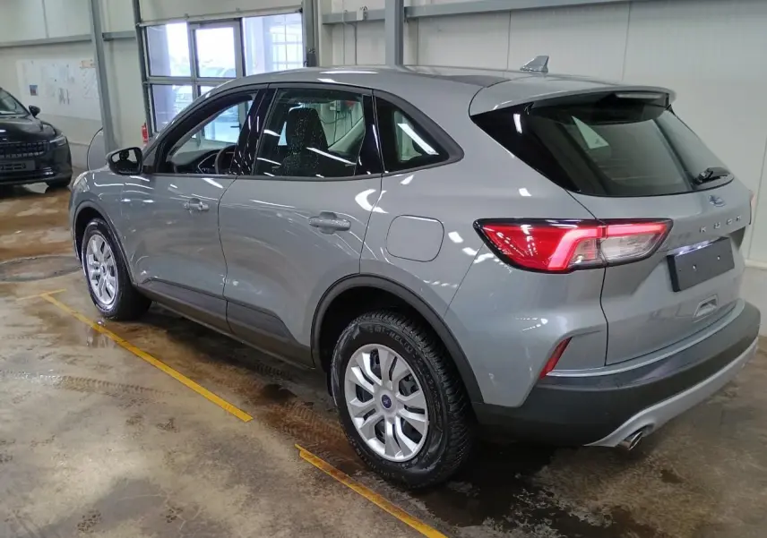Ford Kuga gris Solar vu de 3/4 arrière droit dans un garage, avec feux arrière allumés et jantes argentées.