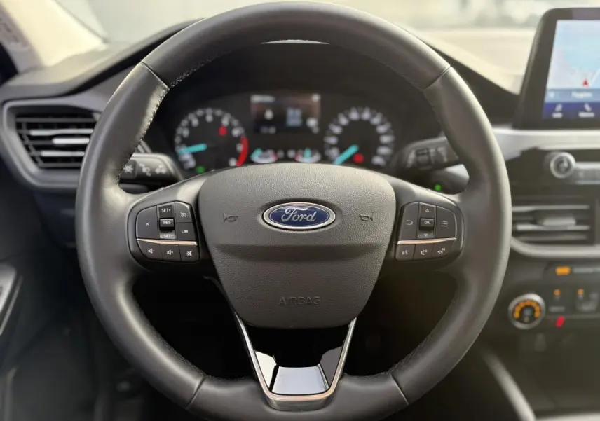 Vue rapprochée du volant multifonctions en cuir noir du Ford Kuga 2024 avec tableau de bord et écran GPS tactile visible.