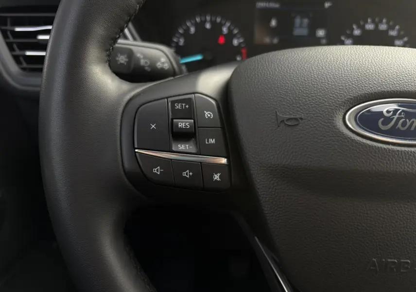 Gros plan sur le volant multifonctions en cuir du Ford Kuga 2024, mettant en valeur les commandes de régulateur et audio.